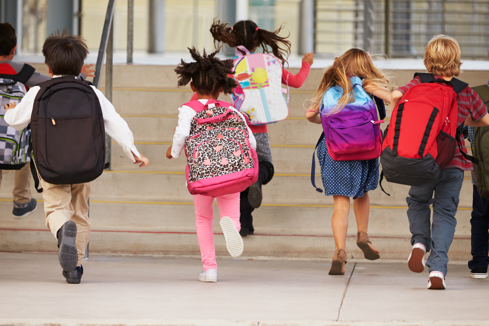 Elementary school children running toward a school building, viewed from behind